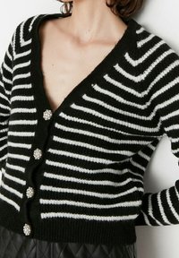 Schwarz-weiß gestreifter Cardigan aus Strickstoff; verfügt über einen V-Ausschnitt, eine Knopfleiste und dekorative Kristallknöpfe.