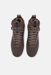 Καφέ ψηλά παπούτσια αθλητικά με υφασμάτινες πάνελ, γκρι κορδόνια και μαύρες λεπτομέρειες. Διαθέτουν επενδυμένο κολάρο και ανθεκτική εξωτερική σόλα.