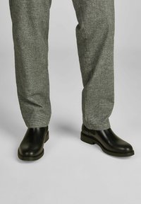 Crne kožne gležnjače s okruglim vrhom i elastičnim bočnim panelima, upotpunjene sivo teksturiranim hlačama.