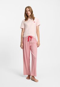 Ανοιχτό ροζ κοντομάνικη μπλούζα με λογότυπο καρδιά, σε συνδυασμό με άνετο, κόκκινο παντελόνι με σχέδια και κόκκινο κορδόνι που ταιριάζει.