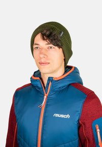 Blue padded jacket with orange accents and maroon sleeves, paired with a green ribbed knit beanie featuring a logo tag on the side.