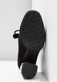 Svart mocka högklackad sko med rund tå, med en texturerad gummisula och en glänsande metallisk hälaccent.