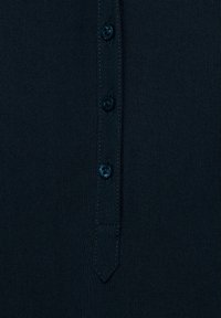 Camicia button-up blu scuro con una pettorina dotata di quattro bottoni blu, texture intrecciata e una leggera lucentezza. Vestibilità sagomata con un design moderno.
