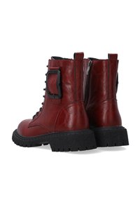 Red leather ankle boots with black rubber soles, featuring a lace-up front, side zipper, and a large buckle accent on the outer side.