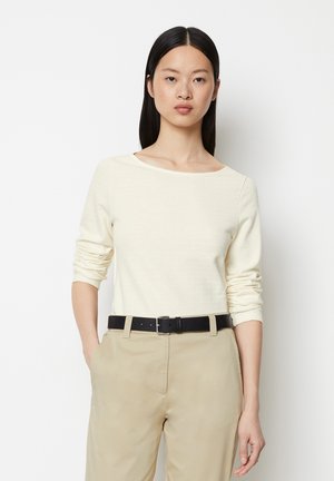 Cremefarbenes Langarmoberteil mit weitem Ausschnitt. Kombiniert mit beigen Hosen und einem schwarzen Gürtel, mit glatter Textur und lässigem Schnitt.