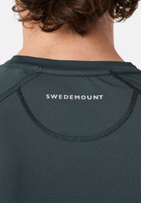 Donkergroen sportshirt van vochtregulerende stof, met ronde halslijn en ademende textuur; heeft het logo "SWEDEMOUNT" op de achterkant.