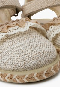 Tkané béžové espadrilky s krajkovým lemem, kulatou špičkou a pletenou jutu podrážkou. Mají texturovanou látku a kontrastní popruhy.