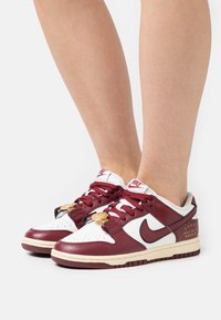 Red and white Nike sneakers with leather upper, round toe, and lace-up closure. Features a gold accessory near the laces and textured accents.
