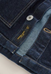 Dark denim jeans featuring a dark blue exterior with contrasting yellow stitching, a black tag marked "DURABLE GOODS," and a metal button.