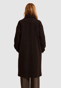 Abrigo largo de lana marrón oscuro con un gran cuello, ajuste ligeramente oversize y patrón texturizado. Presenta hombros caídos y bolsillos laterales.