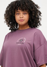 Oversized mauve T-shirt made of cotton with a round neck, featuring a graphic print of a star and text that reads "Celestial Symphony Solar Eclipse."