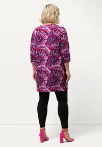 Lang tunika i pink og lilla blomstermønster, med trekvartærmer, parret med sorte leggings og pink højhælede sko. Glat stoftekstur.