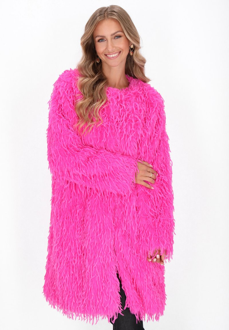 Fluffige roze oversized cardigan met lange mouwen, voorzien van een ruige textuur en een open voorkant, gedragen over donkere broeken.