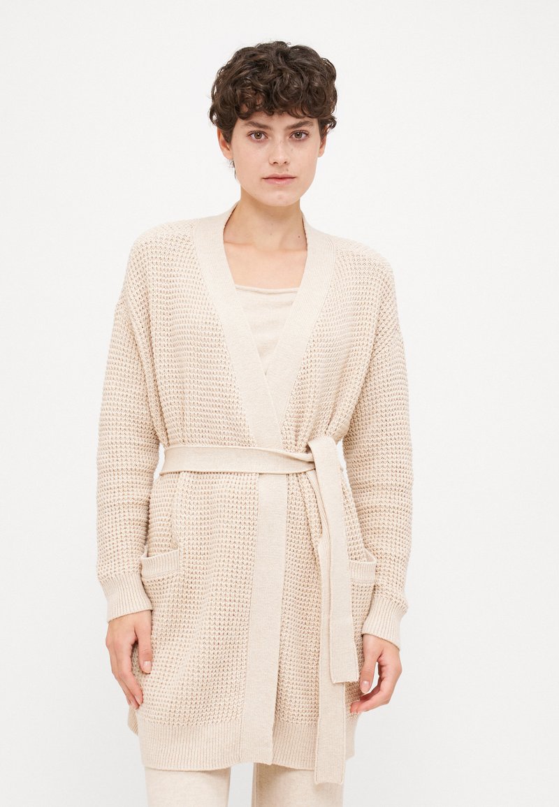 Beige knitted cardigan with a tie belt, long sleeves, two front pockets, and a textured pattern. Lightweight fabric with a loose fit.