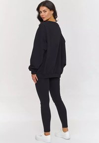 Czarny oversize sweatshirt z długimi rękawami i ściągaczami, w połączeniu z dopasowanymi czarnymi legginsami i białymi sneakersami. Gładka tekstura materiału.