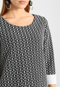 Svart och vit mönstrad topp med rundad halsringning, långa ärmar och vitt manschettdetalj, med en texturerad tyggdesign.