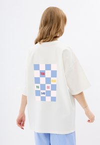 Biała, oversize koszulka z pastelową kratką na plecach oraz napisem: "TOO RAD TO BE SAD" w różnych kolorach.