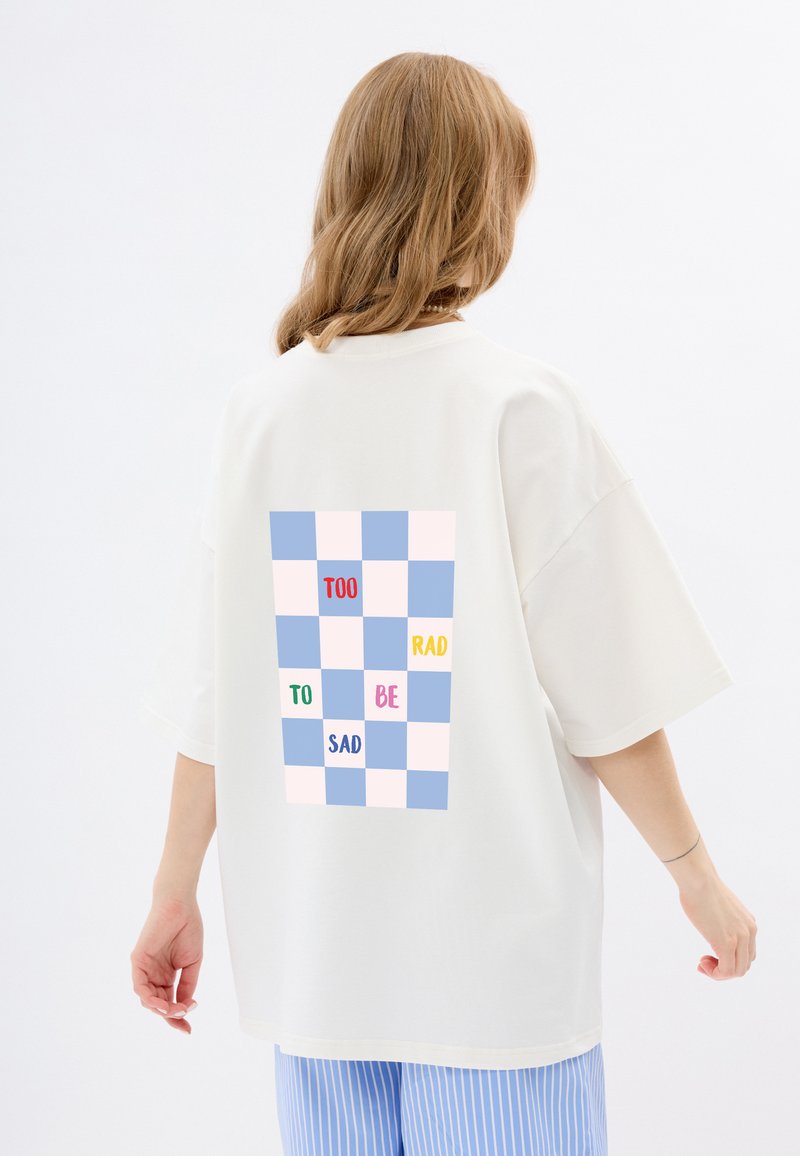 Biała, oversize koszulka z pastelową kratką na plecach oraz napisem: "TOO RAD TO BE SAD" w różnych kolorach.