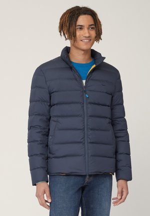 Marineblauwe pufferjas met een ritssluiting, horizontale stiksels en staande kraag. Voorzien van een contrasterende gele voering en blauwe ritslip.