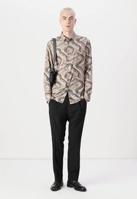Lange mouwen, gestreepte shirt met een beige en bruin slang ontwerp; gecombineerd met zwarte broek en stijlvolle zwarte schoenen.