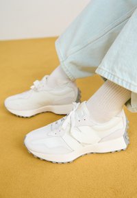 Weiße Sportschuhe mit unterschiedlichen Texturen, darunter glattes Leder und Wildlederakzente, mit einer grauen Sohle und weißen Schnürsenkeln, getragen mit hellblauen Hosen.