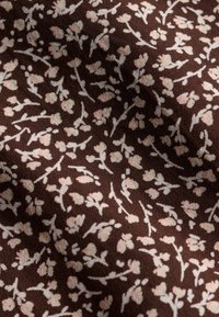 Tissu marron avec un petit motif de branches florales rose clair, montrant la texture et des plis doux.