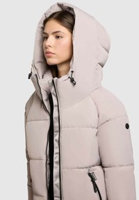 Gevoerde jas in lichtbeige met een hoge kraag en grote capuchon. Voorzien van een ritssluiting aan de voorkant en zijzakken, elastische trekkoorden en een gladde textuur.