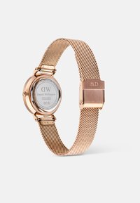 Reloj con correa de malla en dorado rosa que presenta una caja redonda, fondo de cristal y cierre. Las marcas incluyen "DW" y un número de serie en la parte trasera.