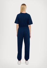 Marineblauwe katoenen trainingspak met korte mouwen en een elastische tailleband; smalle boorden bij de enkels; eenvoudig ontwerp zonder zichtbare patronen of details.
