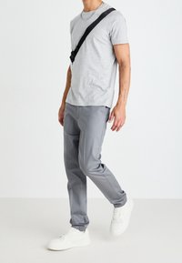 T-shirt grigia a maniche corte abbinata a pantaloni grigi su misura e sneakers bianche. La maglietta presenta un collo tondo; i pantaloni hanno una texture di tessuto liscia.