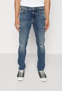 Blå denimjeans med slim fit, med lätt slitningar, framfickor och knäppning. Bärs med svarta högskor.