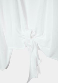 Tissu blanc texturé noué en un nœud lâche, créant des plis drapés et des ombres douces sur un fond clair.