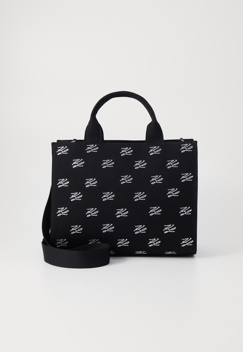 Bolso de tela negro con asas cortas y una correa larga ajustable, que presenta patrones de logotipos blancos repetidos en toda la superficie.