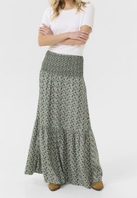 Maxi nederdel i grøn med blomstermønster, der har en smocked talje og lagdelt design. Kombineret med en tætsiddende hvid skjorte og brune støvler.