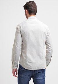 Light grey long-sleeve shirt with a back yoke, subtle texture, and buttoned cuffs, paired with dark blue denim jeans.
