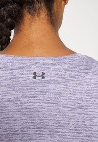 Lila sporttröja med en slät textur, med ett subtilt randmönster och en svart logotyp på baksidan nära nacke.