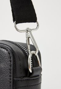 Coin du sac en cuir noir présentant une fermeture éclair en métal et des accessoires en argent. Surface texturée avec une sangle tissée noire et un fermoir robuste.