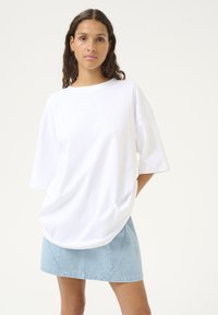 Witte oversized t-shirt met korte mouwen, een ronde halslijn en zachte katoenen stof. Gecombineerd met een lichtblauwe denim mini-jurk.