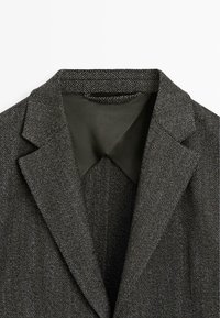Blazer grigio scuro con motivo pied de poule e collo a lancia, caratterizzato da una fodera interna liscia e un esterno strutturato.