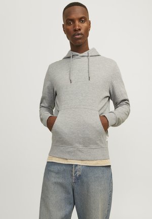 Gray hoodie with drawstring, front pocket, and ribbed hem. Worn over a light-colored layered shirt. Distressed blue jeans.