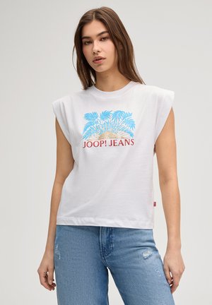 Frau trägt ein weißes ärmelloses Oberteil mit blauem Palmen- und Sonnenmotiv und rotem "JOOP! JEANS"-Schriftzug, kombiniert mit hellblauen Jeans.