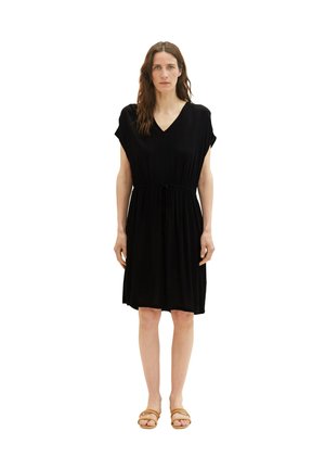 Schwarzes knielanges Kleid mit V-Ausschnitt, kurzen Ärmeln und einer Kordelzug-Taille. Getragen mit hellbraunen flachen Sandalen. Glatte Textur, einfaches Design.