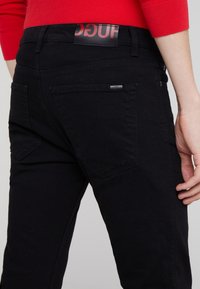 Svarta denimjeans med midje i medelhöjd, bakfickor och en märkesflik i midjan. Slät textur med en åtsittande silhuett.