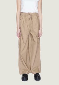 Pantaloni beige a gamba larga con vita regolabile e tasche laterali; realizzati in tessuto leggero; abbinati a scarpe con zeppa nere.