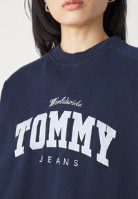 Sudadera de marina con estampado en blanco audaz de "TOMMY", con "Worldwide" arriba y "JEANS" abajo, cuello de crew ribeteado y tejido texturizado.