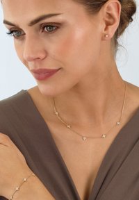 Goldfarbene Schmuckset mit einer zarten Halskette und passenden Ohrringen. Jedes Stück hat kleine florale Designs, die mit funkelnden Steinen akzentuiert sind.