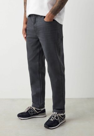 Dunkelgraue Jeans für Herren aus Denim, mit klassischer Passform, Seitentaschen und einem schlichten Design. Kombiniert mit schwarzen Sportschuhen.
