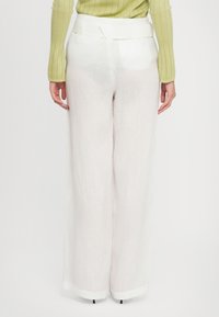 White linen wide-leg pants with a smooth, light texture and a waistband. The pants have a clean finish at the hems and minimal detailing.