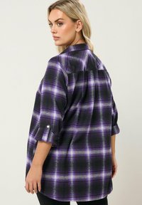 Musta ja violetti ruudullinen nappipaita, jossa on käärityt hihat, takaniitti ja rento istuvuus. Pehmeä kangas harjatulla tekstuurilla.