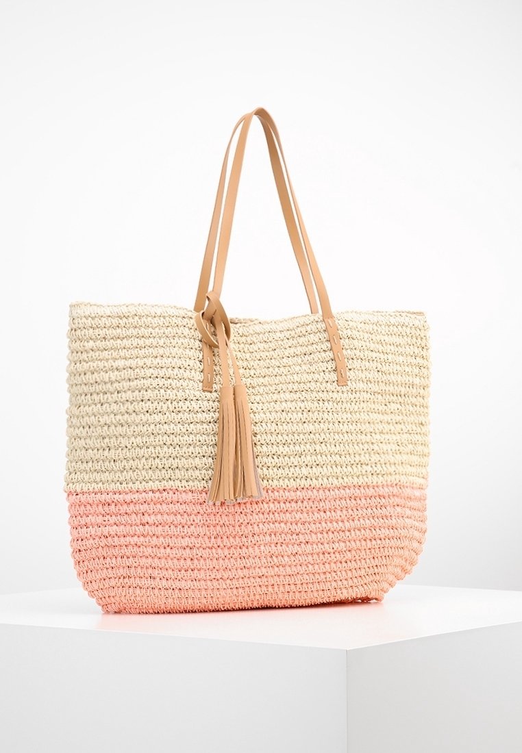 Vävd halm tote-väska med en beige övre del och en korallrosa botten. Har två tan läderremmar och en tofsaccent.